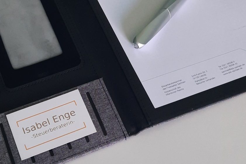 Ein klarer Ordner mit einer Visitenkarte und einem Stift, neben weißem Papier.